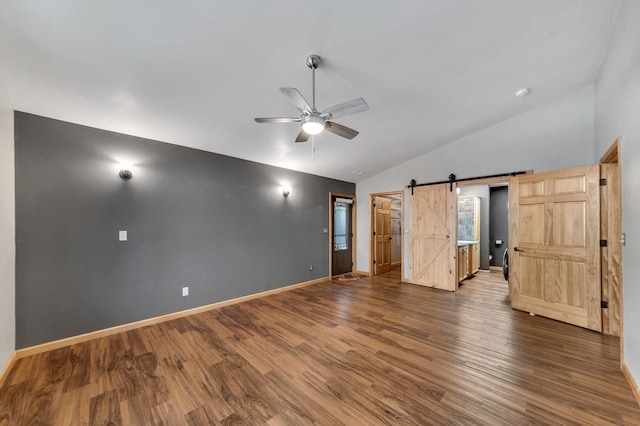 unfurnished bedroom with hardwood / wood-style flooring, ceiling fan, a barn door, and lofted ceiling