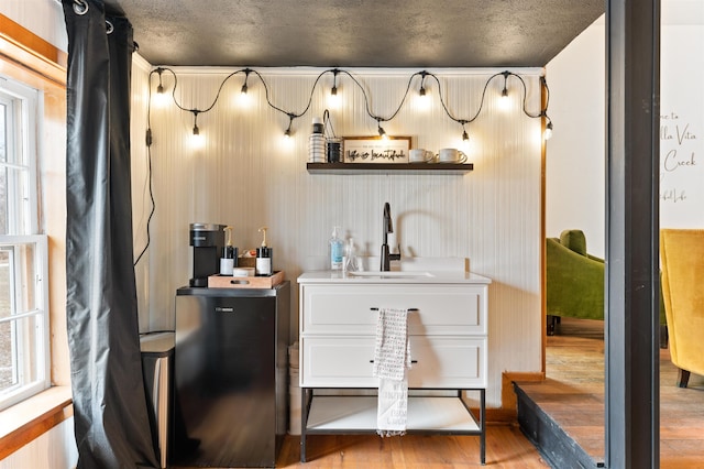 bar featuring hardwood / wood-style flooring, wood walls, sink, and a textured ceiling