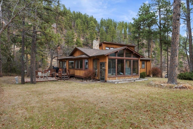 back of house with a sunroom, a wooden deck, and a lawn