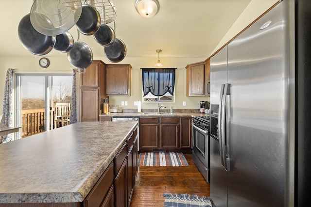 kitchen with appliances with stainless steel finishes, dark hardwood / wood-style flooring, sink, a center island, and hanging light fixtures