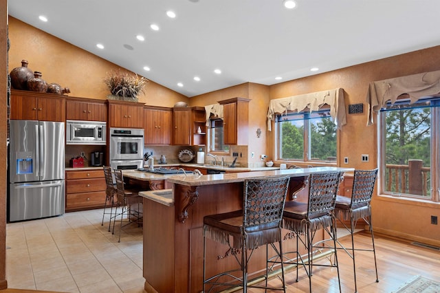 kitchen with light stone countertops, kitchen peninsula, lofted ceiling, a kitchen bar, and appliances with stainless steel finishes