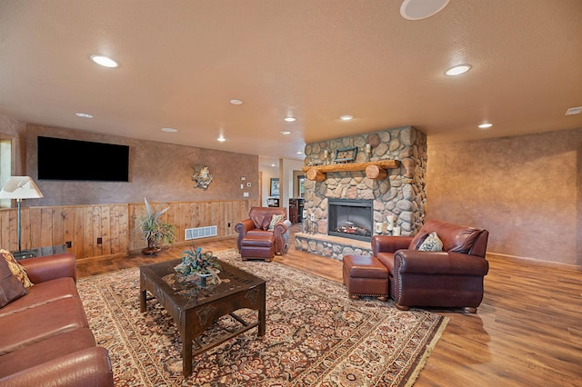 living room featuring a stone fireplace, wooden walls, wood-type flooring, and a textured ceiling