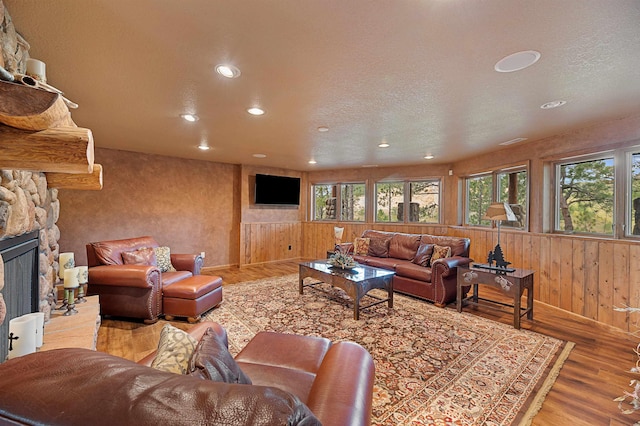 living room with a fireplace, light wood-type flooring, a textured ceiling, and wooden walls