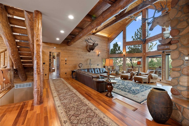 living room featuring log walls, beamed ceiling, light hardwood / wood-style floors, and a high ceiling