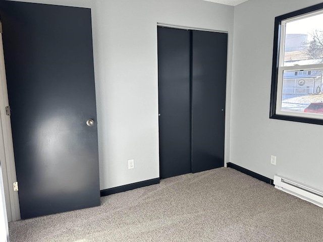 unfurnished bedroom with light carpet, a closet, and a baseboard heating unit