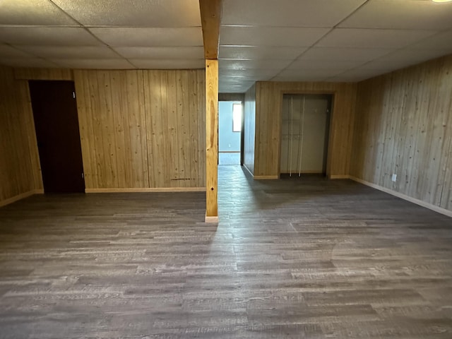 spare room featuring a drop ceiling, dark wood-type flooring, and wooden walls