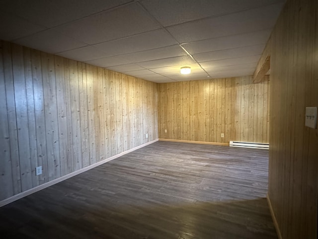 basement with a paneled ceiling, wooden walls, a baseboard radiator, and dark wood-type flooring