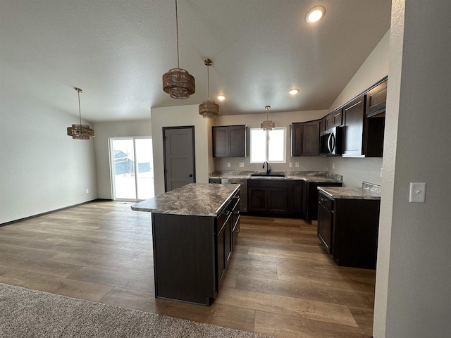 kitchen with stainless steel microwave, light wood-style flooring, a sink, a kitchen island, and dark brown cabinetry