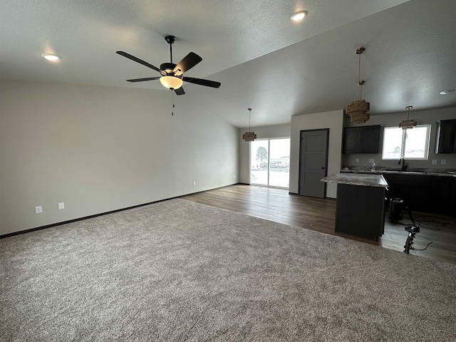 unfurnished living room featuring wood finished floors, a sink, a ceiling fan, vaulted ceiling, and carpet