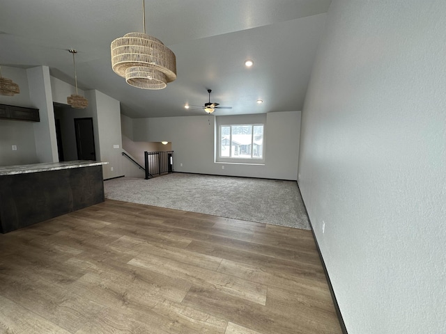 unfurnished living room with light colored carpet, ceiling fan with notable chandelier, baseboards, vaulted ceiling, and light wood finished floors