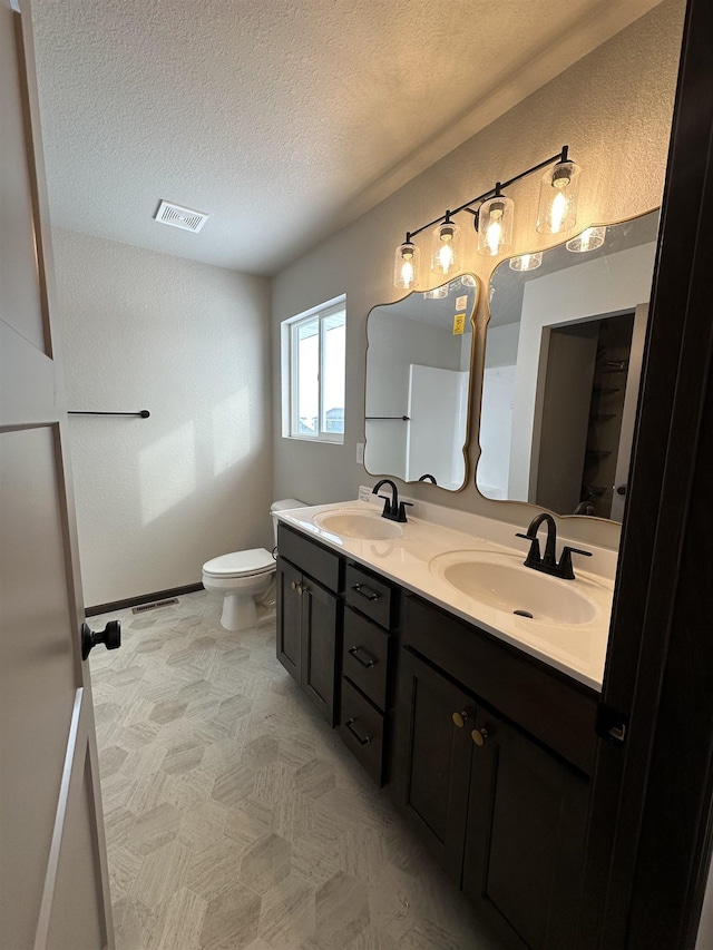 bathroom with a textured ceiling, toilet, a sink, and visible vents