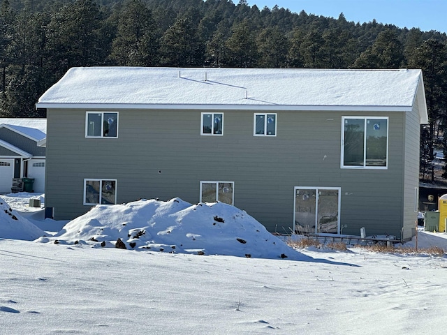 snow covered rear of property featuring a view of trees