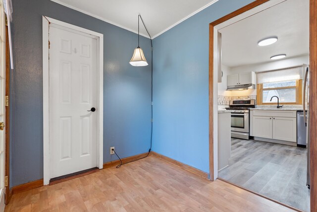 unfurnished dining area with light wood-type flooring, ornamental molding, and sink