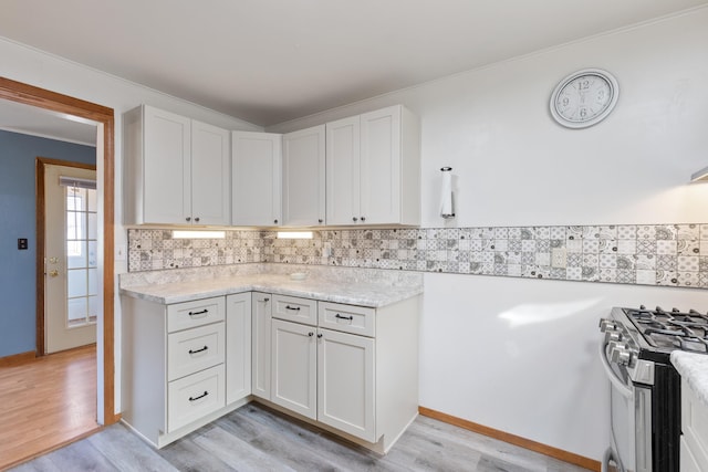 kitchen with light wood-type flooring, backsplash, crown molding, white cabinetry, and stainless steel range with gas stovetop