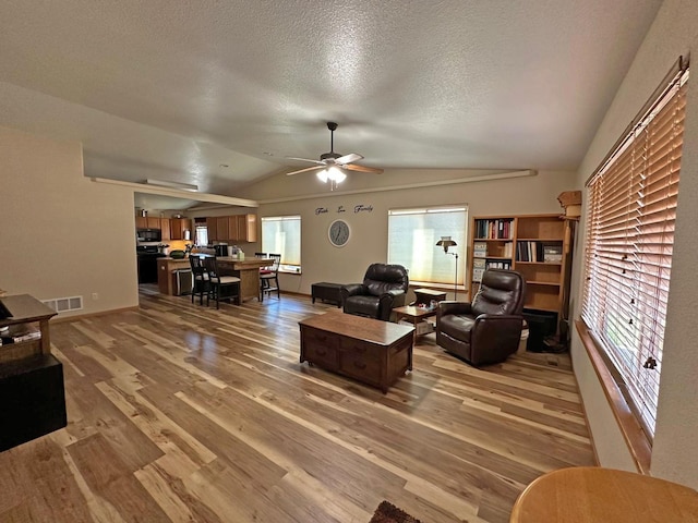 living room with ceiling fan, plenty of natural light, wood-type flooring, and lofted ceiling