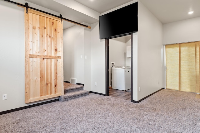 unfurnished bedroom featuring dark colored carpet, independent washer and dryer, a barn door, and ensuite bath