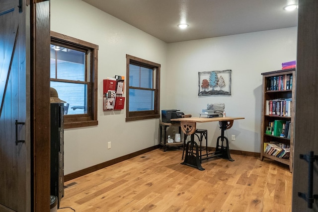 home office with a barn door and light hardwood / wood-style floors