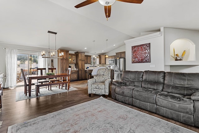 living room featuring ceiling fan with notable chandelier, dark wood-type flooring, and vaulted ceiling