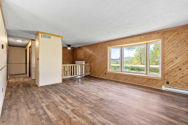 interior space with a textured ceiling, ceiling fan, wooden walls, a baseboard heating unit, and hardwood / wood-style flooring