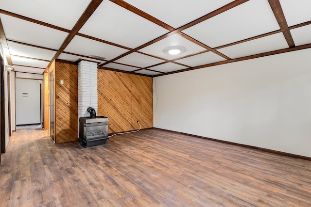 unfurnished living room featuring a wood stove, dark wood-type flooring, coffered ceiling, beamed ceiling, and wooden walls