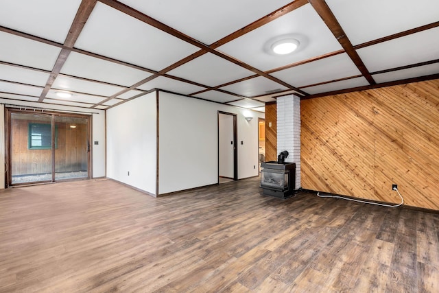 unfurnished living room featuring a wood stove, coffered ceiling, beamed ceiling, wood walls, and hardwood / wood-style floors