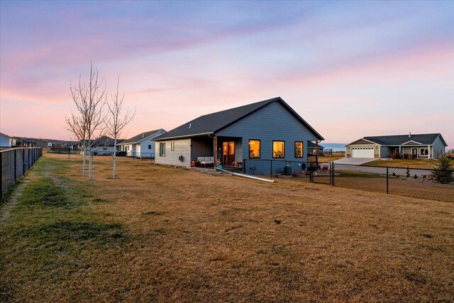 back house at dusk with a lawn and a garage