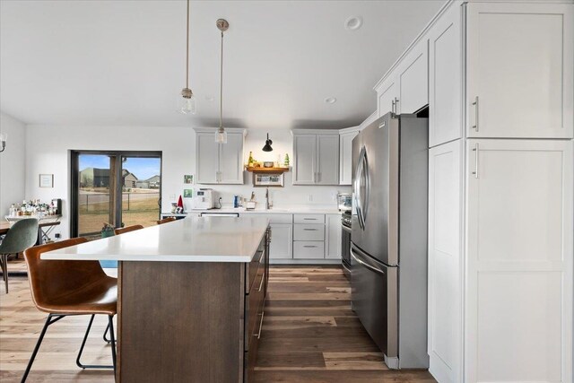 kitchen with a center island, hanging light fixtures, dark hardwood / wood-style flooring, stainless steel fridge, and a kitchen bar