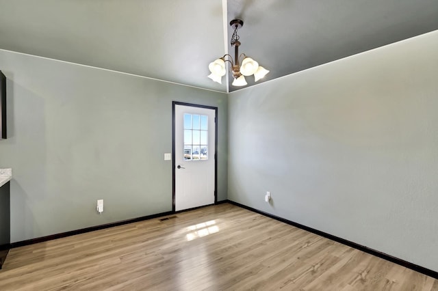 spare room with a chandelier and light wood-type flooring