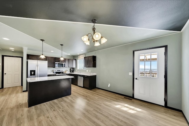 kitchen with pendant lighting, lofted ceiling, appliances with stainless steel finishes, dark brown cabinets, and a kitchen island