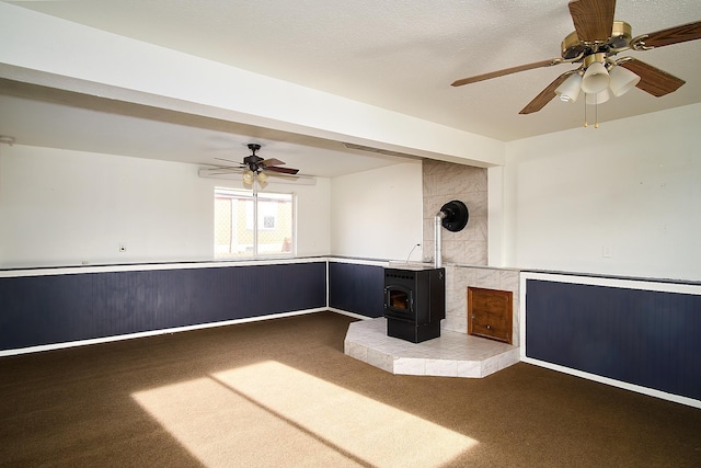 carpeted empty room with a wood stove and ceiling fan