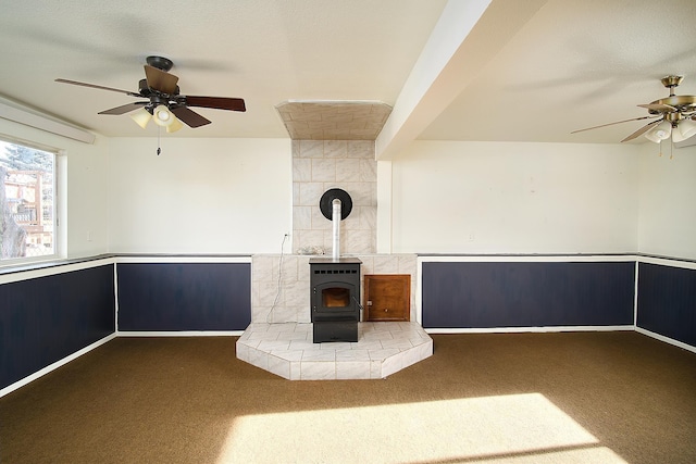 unfurnished living room featuring carpet flooring, a wood stove, and ceiling fan