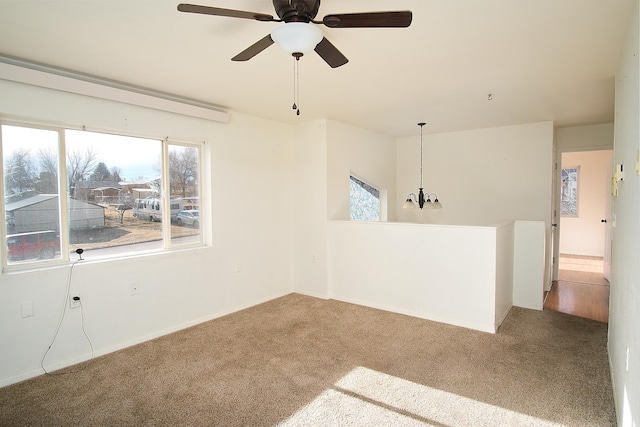 carpeted empty room featuring ceiling fan with notable chandelier