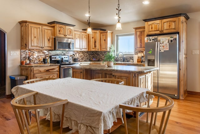 kitchen featuring light hardwood / wood-style floors, decorative light fixtures, vaulted ceiling, a kitchen island, and appliances with stainless steel finishes