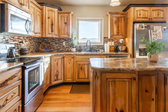 kitchen with decorative backsplash, appliances with stainless steel finishes, light stone counters, sink, and light hardwood / wood-style flooring