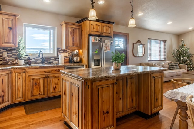 kitchen with sink, light hardwood / wood-style flooring, stainless steel fridge with ice dispenser, a center island, and hanging light fixtures