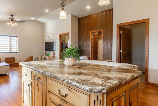 kitchen with pendant lighting, vaulted ceiling, ceiling fan, light wood-type flooring, and light stone counters