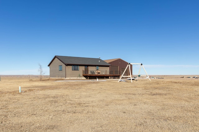 back of property with a playground, a rural view, and a deck