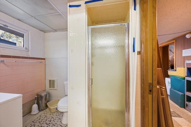 bathroom with a drop ceiling, washer / dryer, toilet, a shower with door, and tile walls