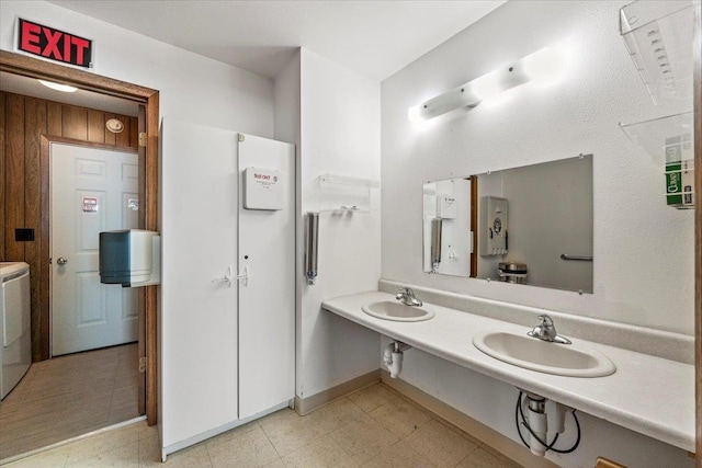 bathroom with dual sinks and wood walls