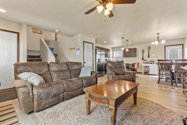 living room featuring ceiling fan with notable chandelier and light wood-type flooring