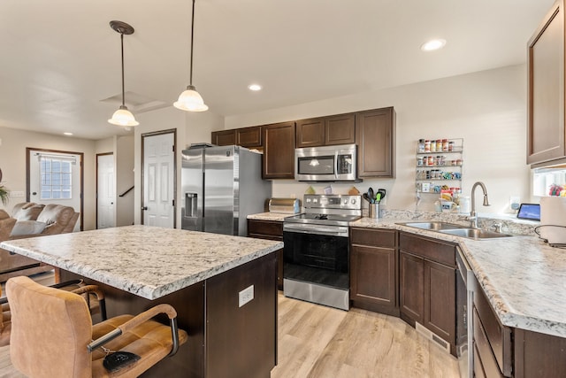 kitchen featuring sink, hanging light fixtures, stainless steel appliances, light hardwood / wood-style flooring, and a kitchen bar