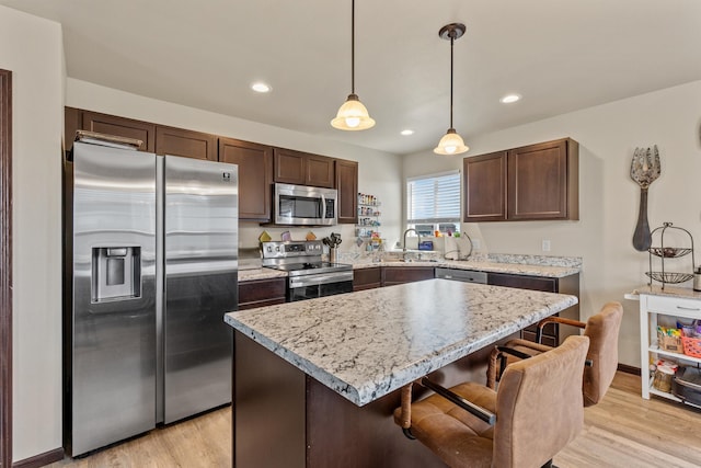 kitchen featuring light hardwood / wood-style flooring, a kitchen island, pendant lighting, and appliances with stainless steel finishes