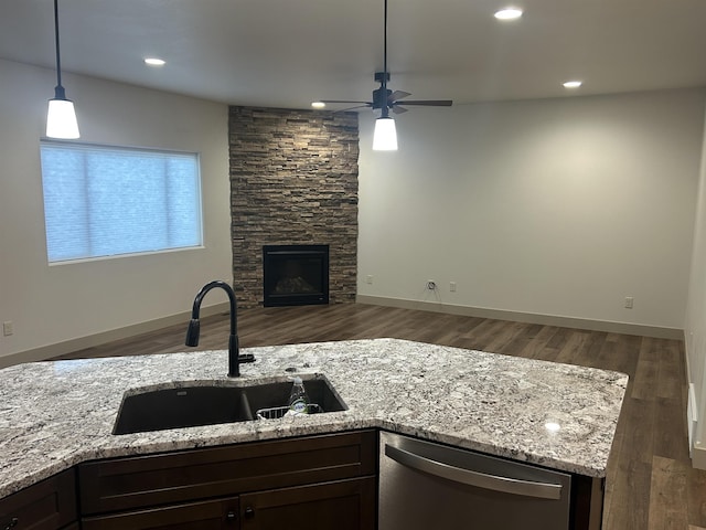 kitchen with light stone countertops, dishwasher, sink, hanging light fixtures, and a stone fireplace