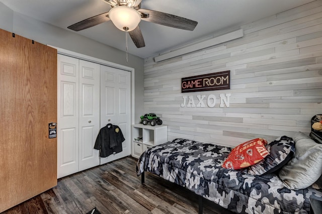 bedroom featuring ceiling fan, wood walls, dark hardwood / wood-style flooring, and a closet