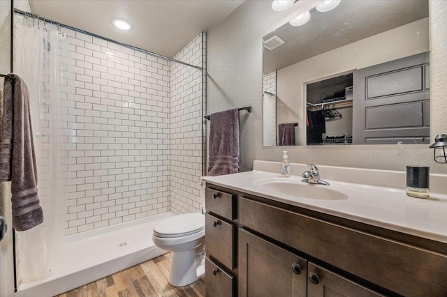 bathroom with hardwood / wood-style floors, vanity, toilet, and tiled shower