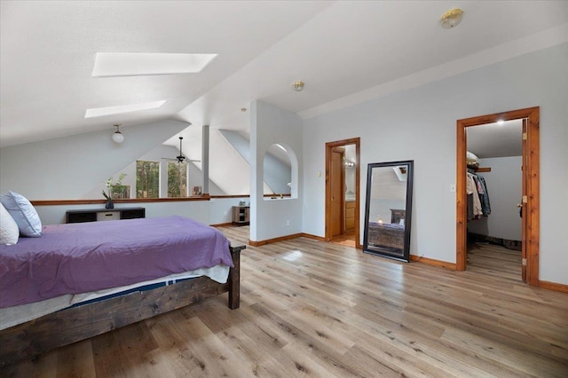 bedroom featuring connected bathroom, light hardwood / wood-style floors, a spacious closet, and vaulted ceiling with skylight