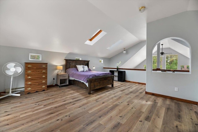 bedroom with light hardwood / wood-style flooring, a baseboard heating unit, and vaulted ceiling with skylight