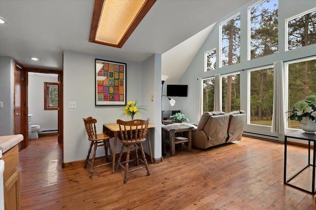 dining room featuring lofted ceiling with skylight, hardwood / wood-style floors, and a baseboard radiator