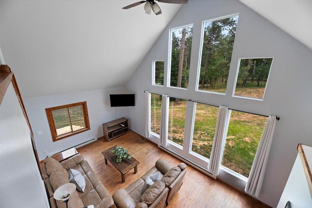 living room featuring ceiling fan, light wood-type flooring, baseboard heating, and a high ceiling