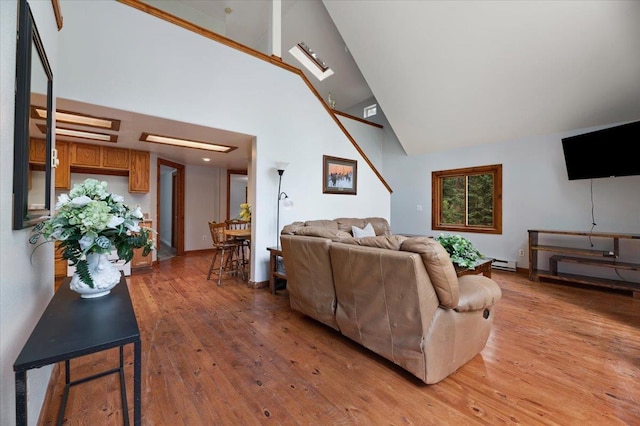 living room with high vaulted ceiling, light hardwood / wood-style flooring, and baseboard heating